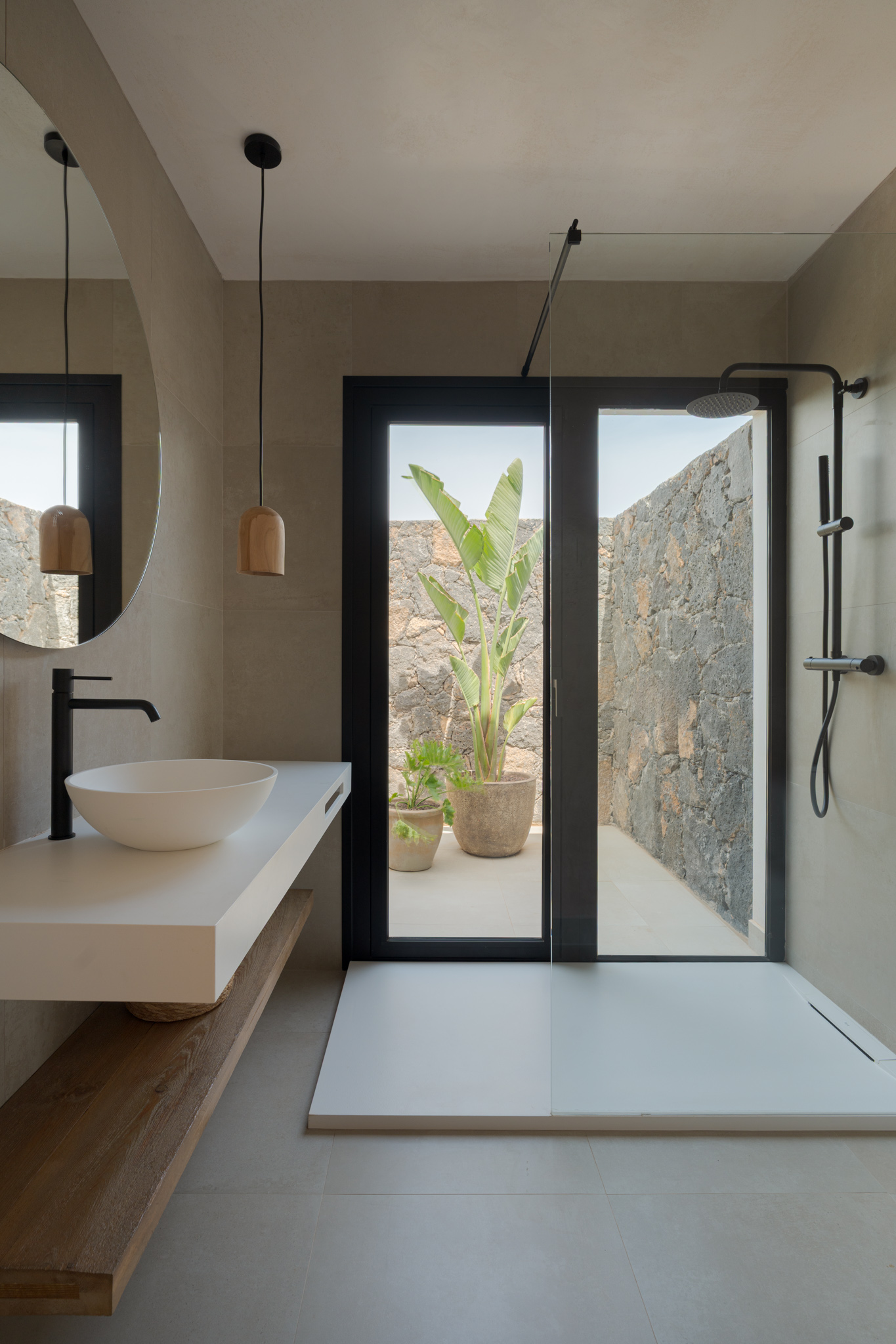Bathroom with white basin, round mirror, wooden pendant light and walk-in shower with garden view